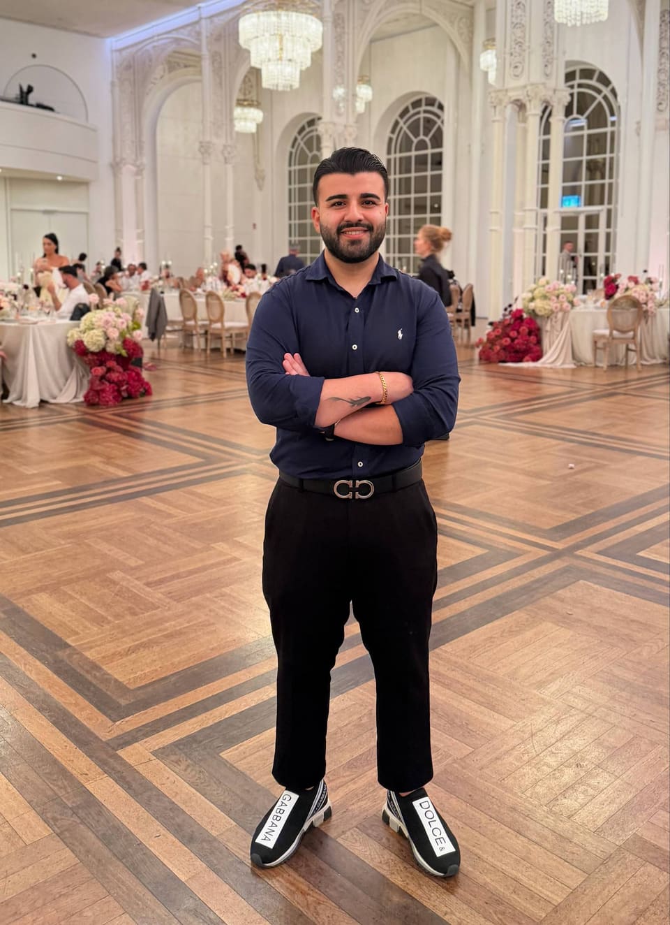 DJ Amir Champ steht auf der Tanzfläche eines Hochzeitssaals mit Kronleuchtern und Blumendekoration